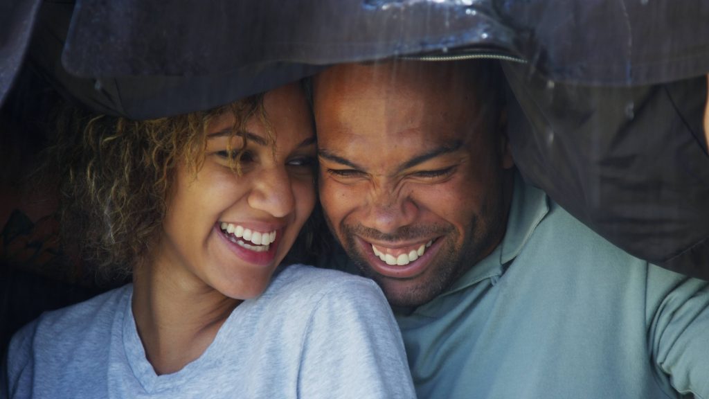 a young, happy African-American couple smiling and covering up in the rain