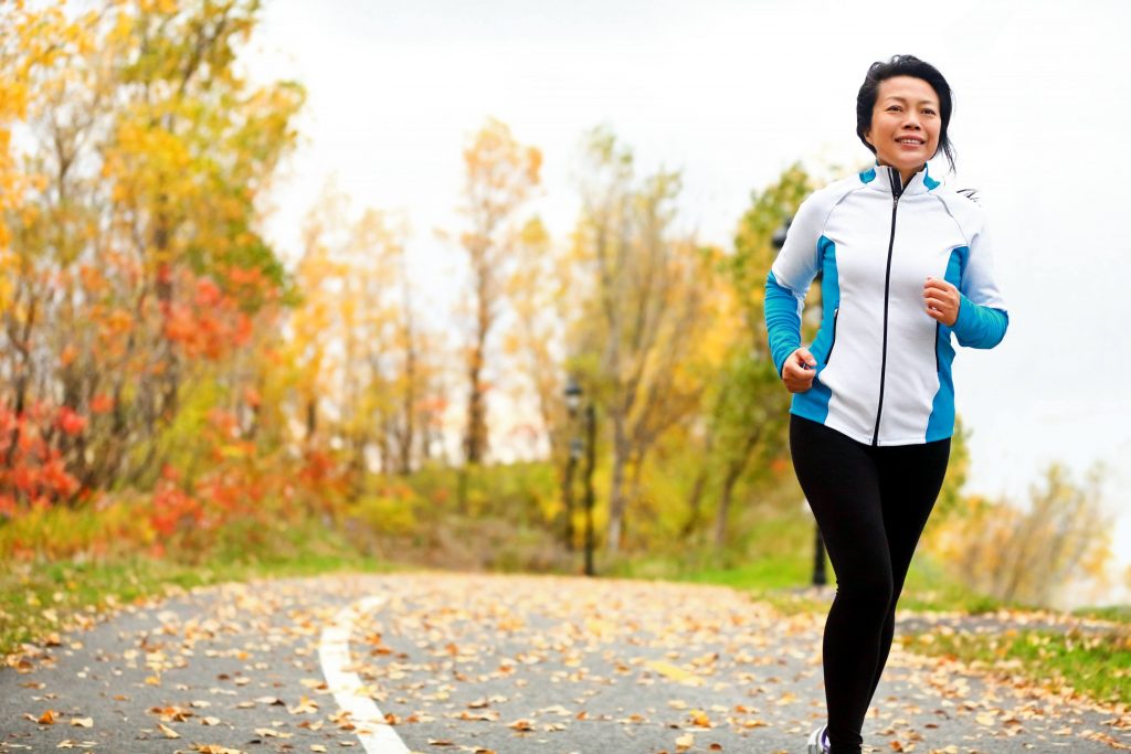a healthy Asian woman exercising and running on street covered in fallen autumn leaves
