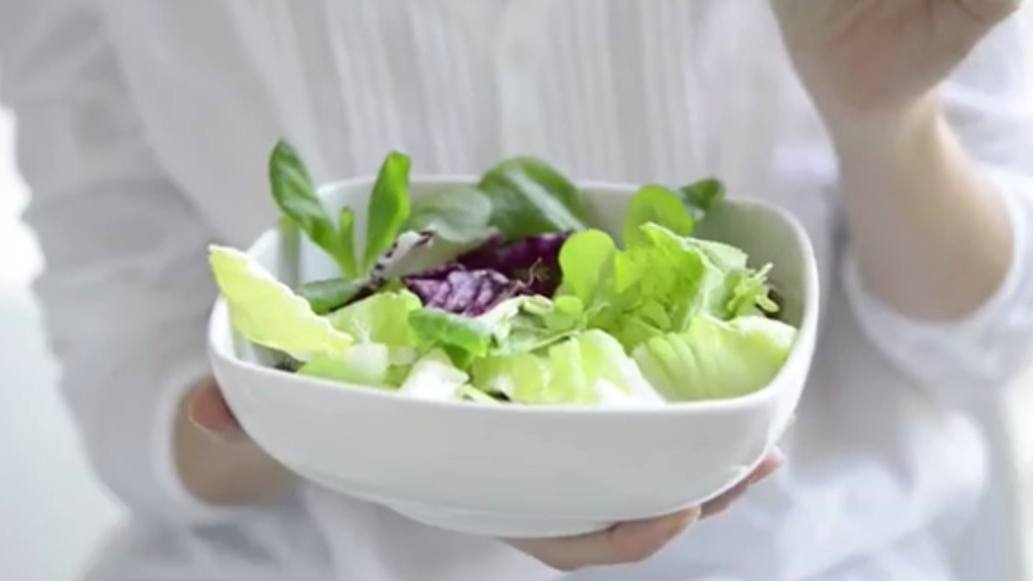 a person holding a fresh green vegetable salad in a white bowl