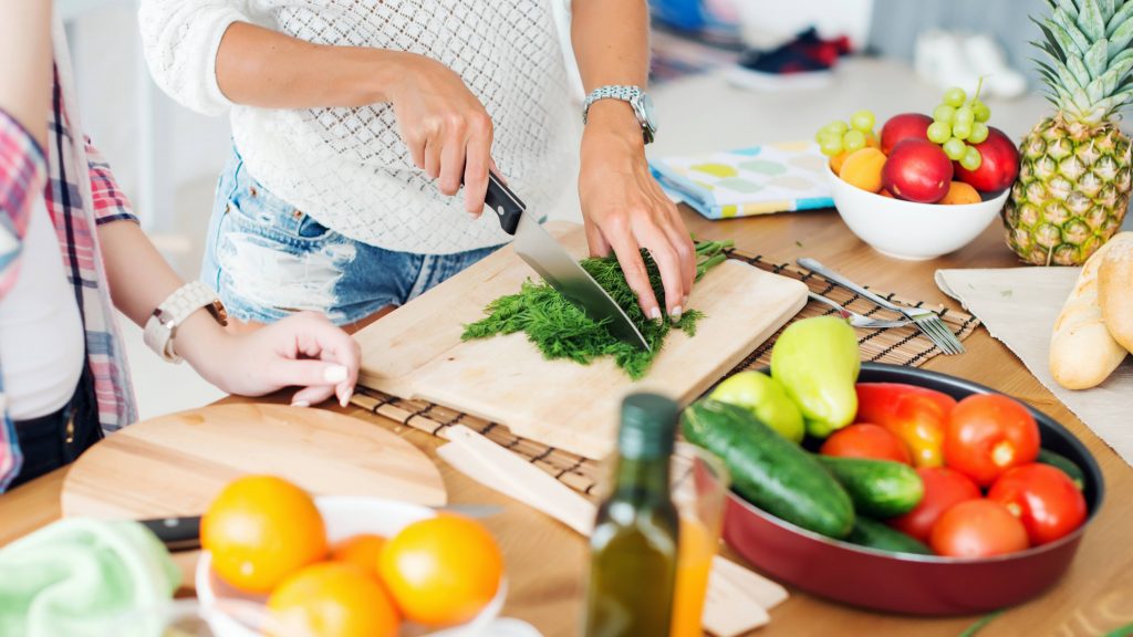 a woman slicing and cutting up fresh fruits and vegetables on a kitchen counter