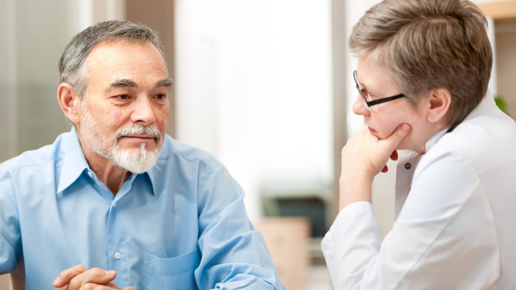 an older man, looking worried or thoughtful, talking with a female health care provider