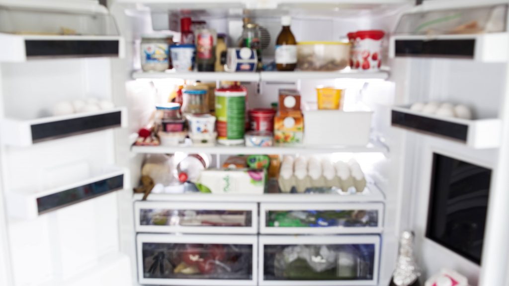 an out-of-focus close-up of the inside of a very full and disorganized refrigerator. Eating habits