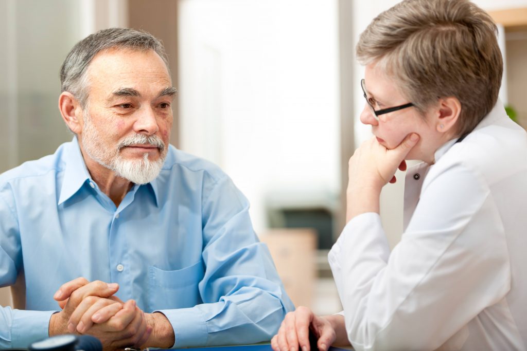 an older man, looking worried or thoughtful, talking with a female health care provider