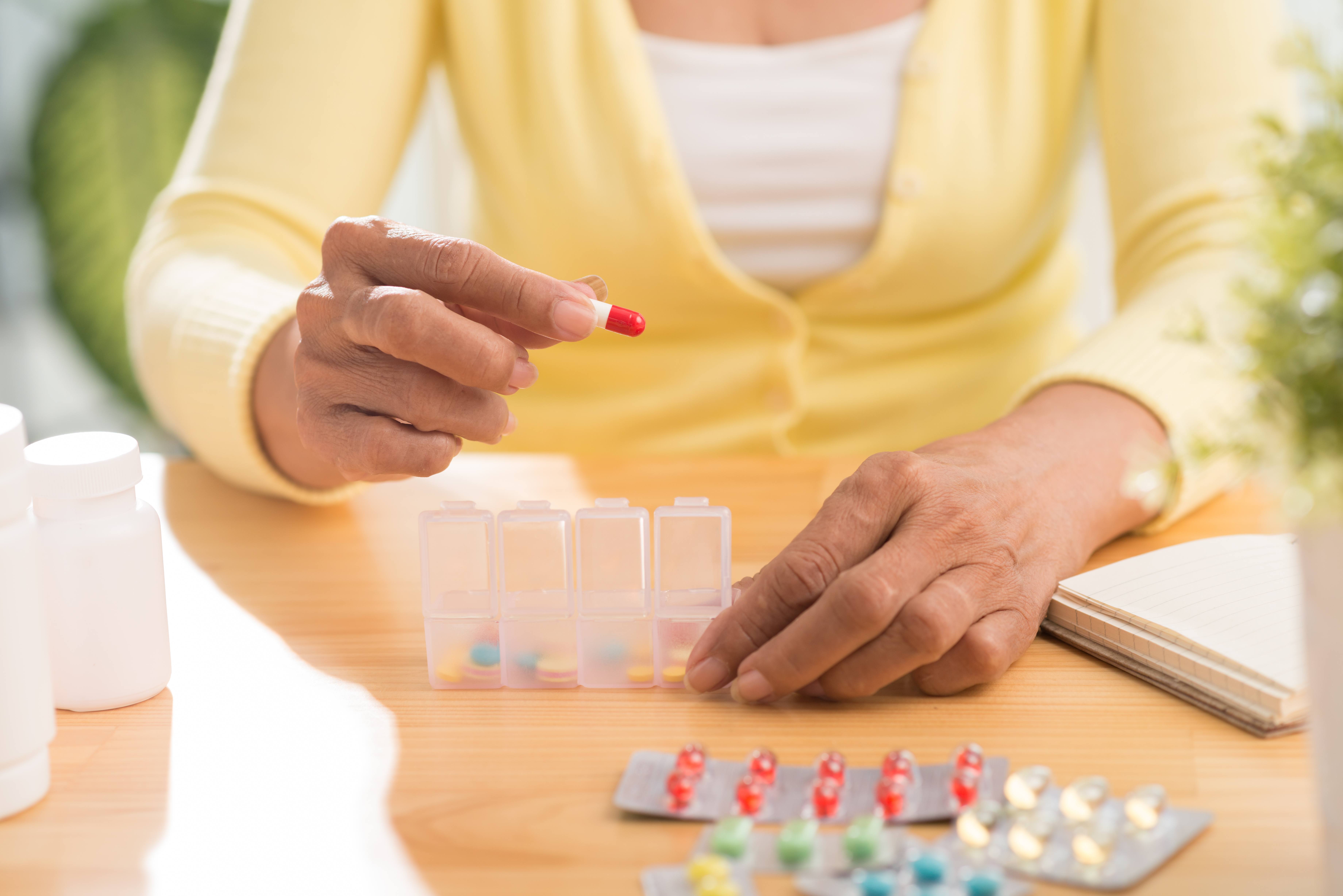 a woman in a yellow sweater sitting at a table with her prescription medicine and putting her pills in a pillbox