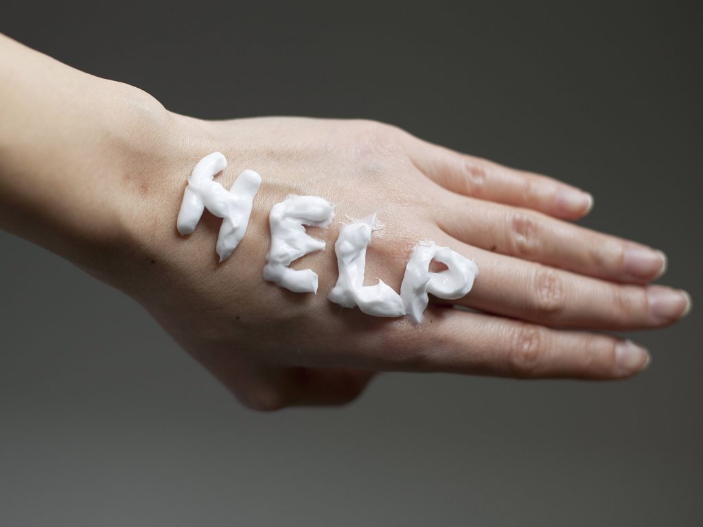 a close-up of the back of a woman's hand with the word help written in lotion