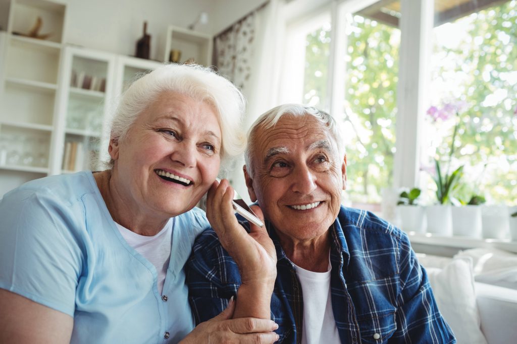an older man and woman smiling and listening together to a cell phone