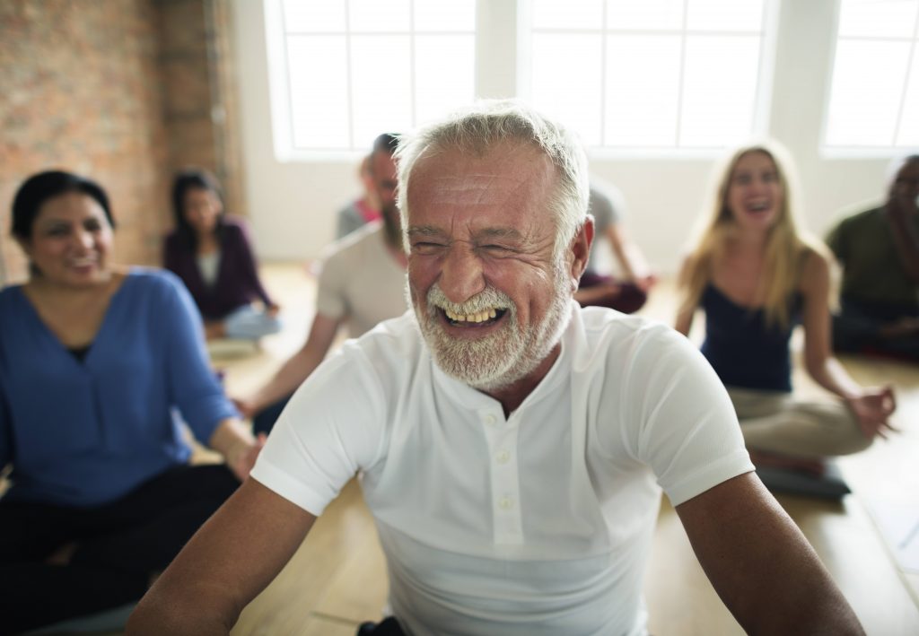 a group of smiling, laughing men and women in a yoga class