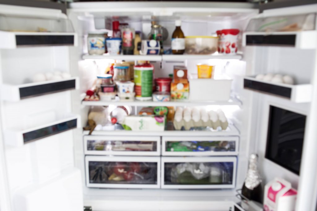 an out-of-focus close-up of the inside of a very full and disorganized refrigerator