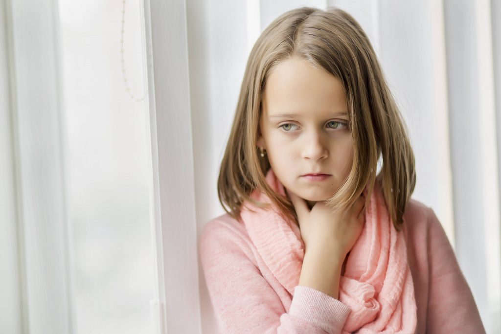 a little girl looking sad and sick, holding her sore throat