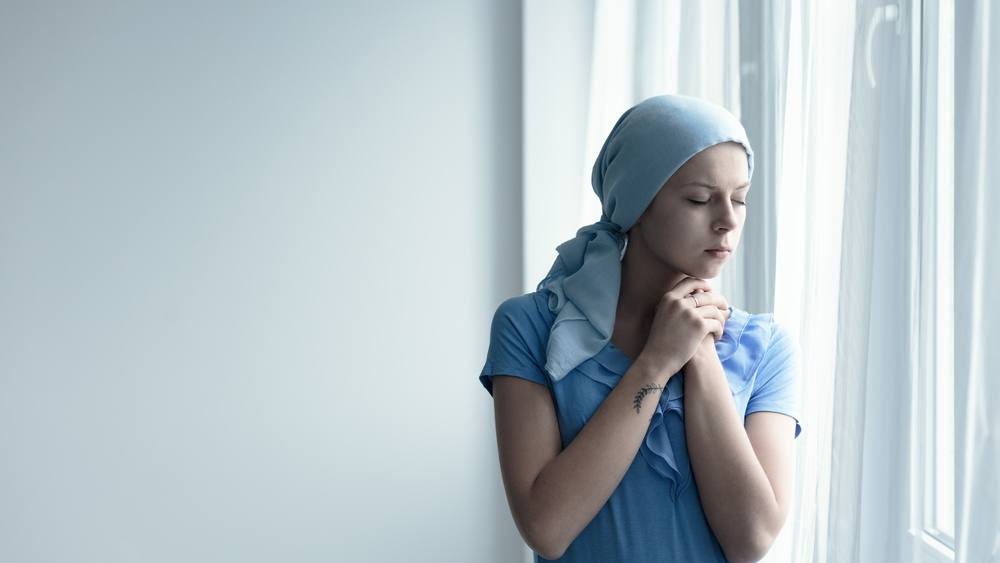 Mujer joven y superviviente de cáncer muy pensativa frente a una ventana