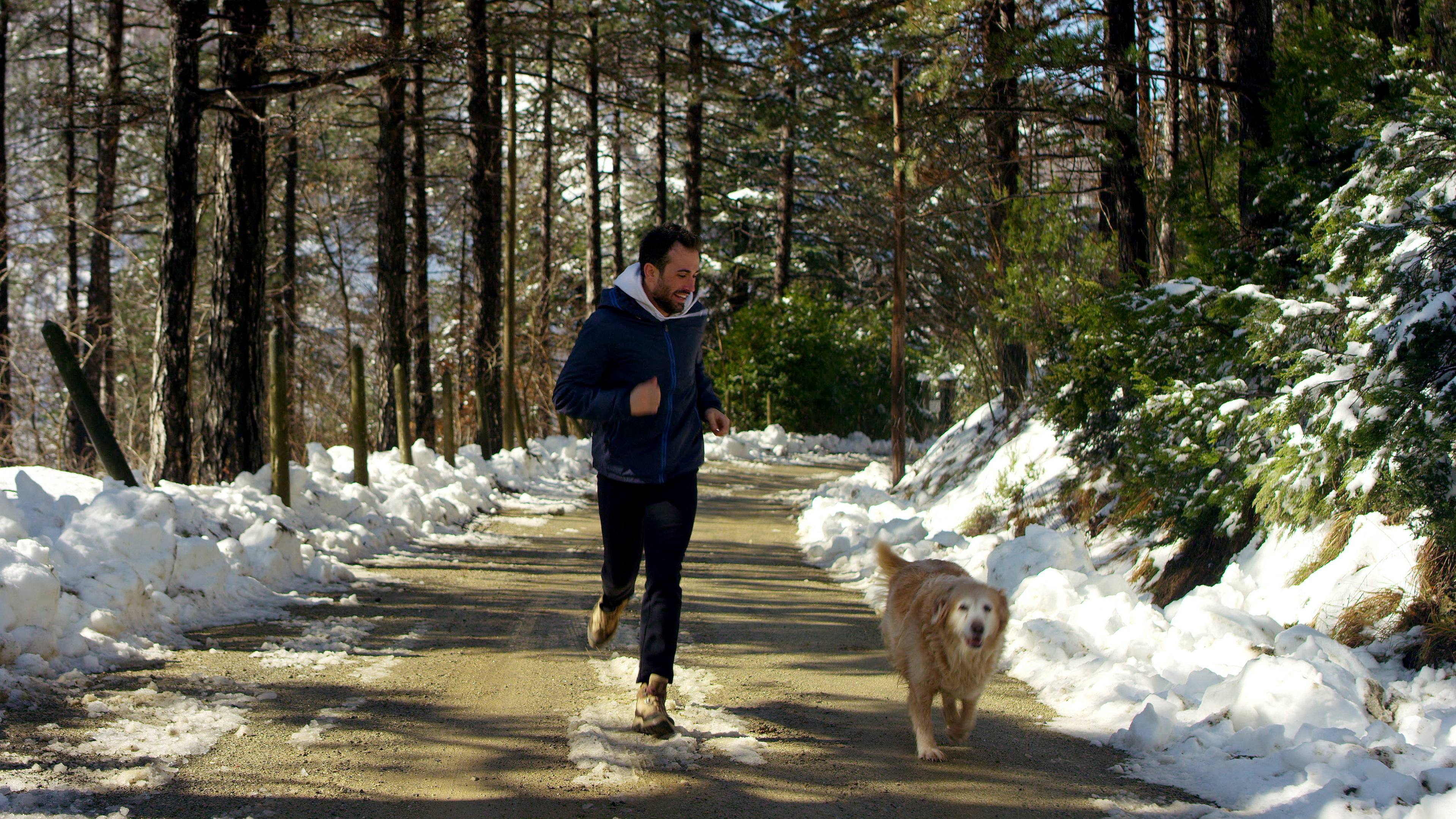 a young man exercising and running with is dog down a dirt path with snow along the road in winter