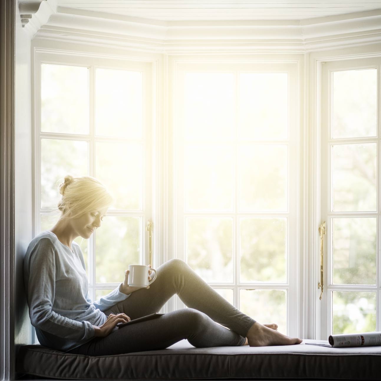 adult woman relaxing in window seat while drinking coffee