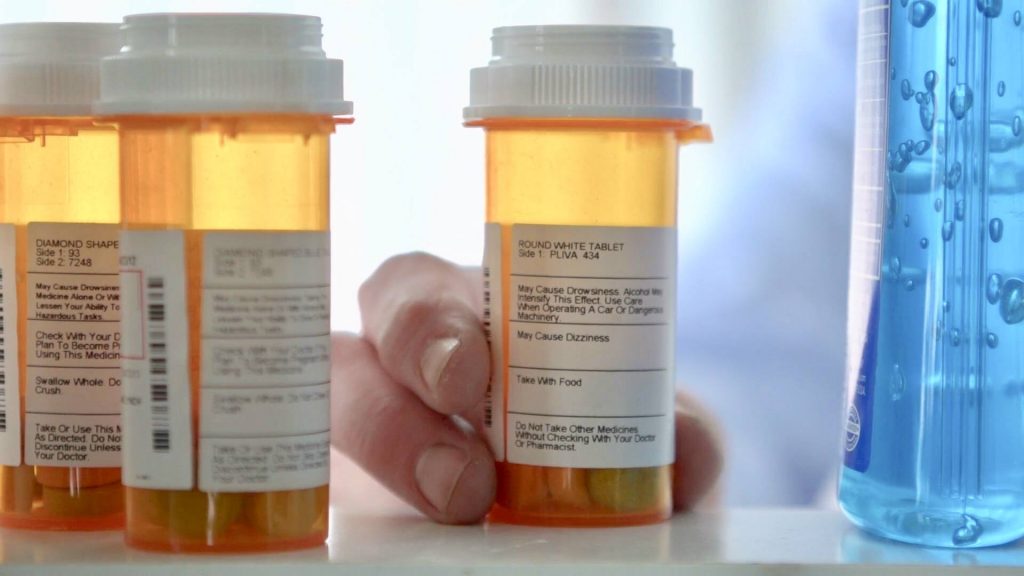 a medicine cabinet with several prescription and medications pill bottles and a person taking one of them out of the cabinet