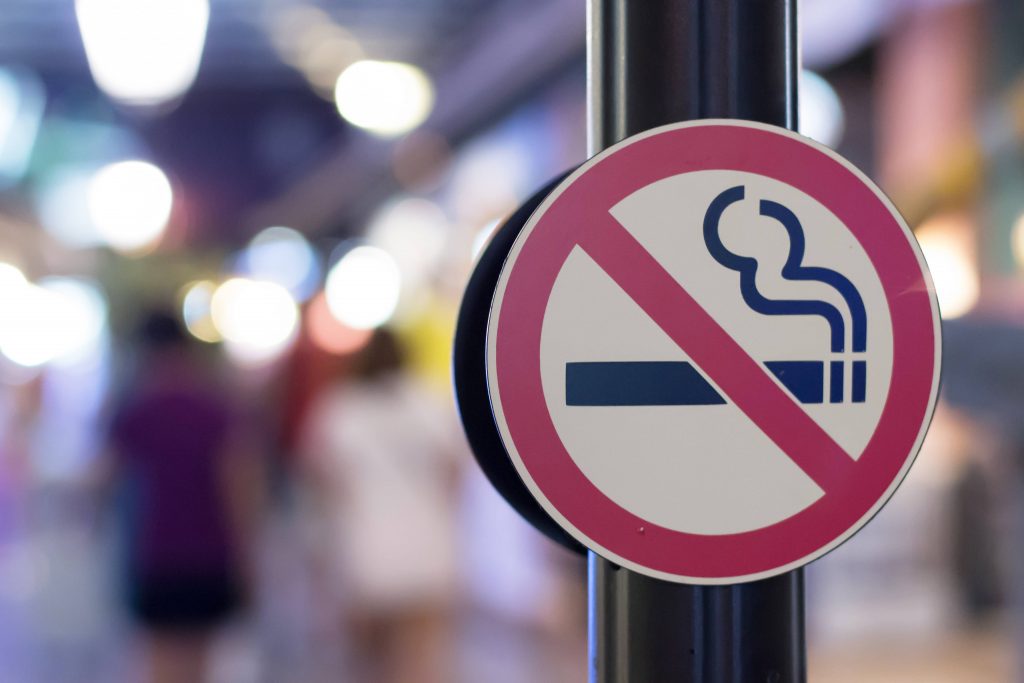 a close-up of a No Smoking symbol on a sign along a busy city sidewalk