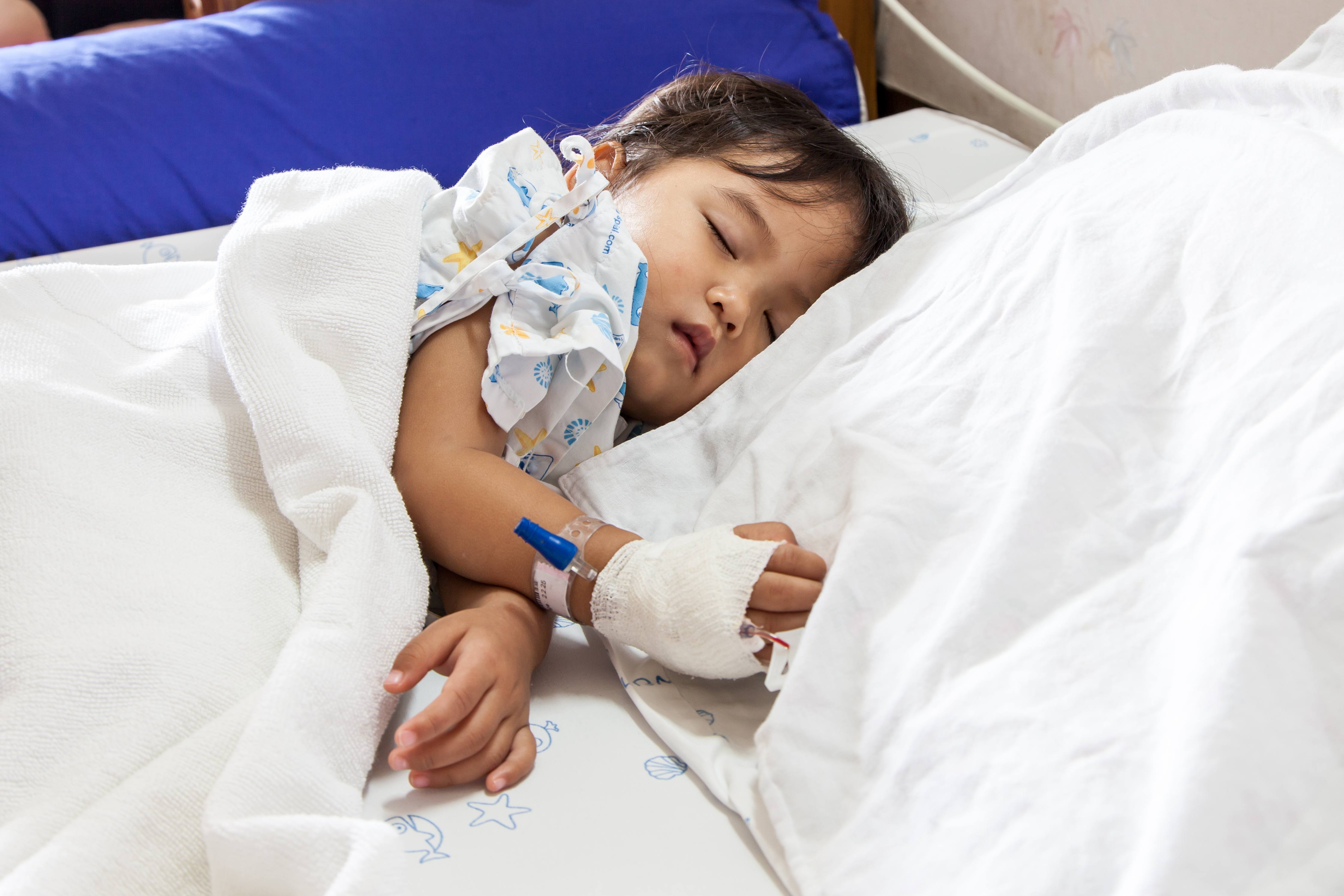 a sick child sleeping in a hospital bed with an IV in his or her hand