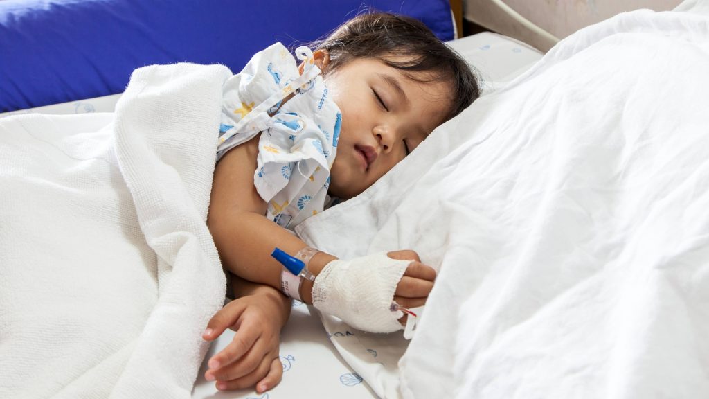a sick child sleeping in a hospital bed with an IV in his or her hand