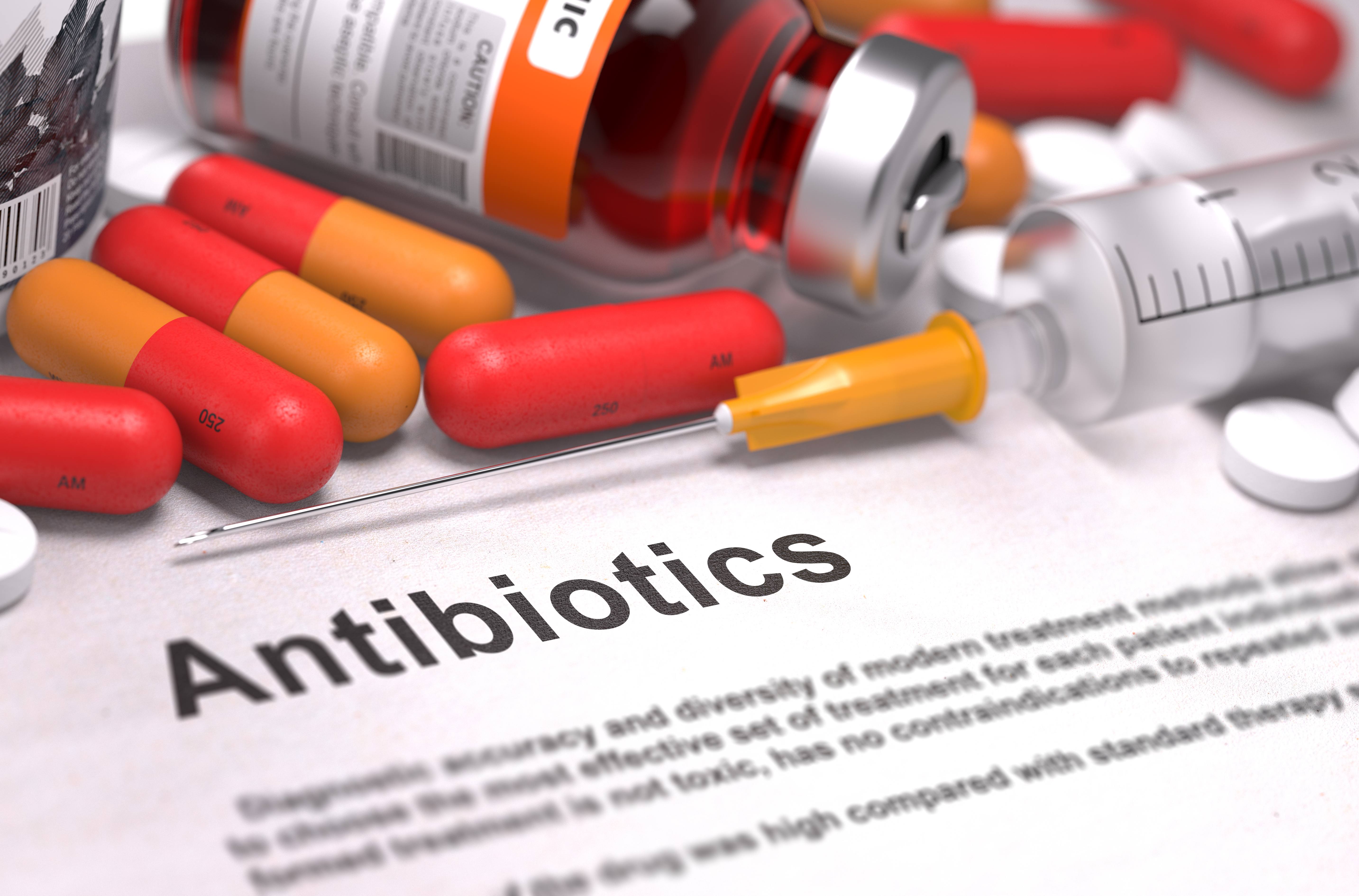 medication bottles, tablets, capules and a syringe spilled out on a piece of paper with the word Antibiotics written on it