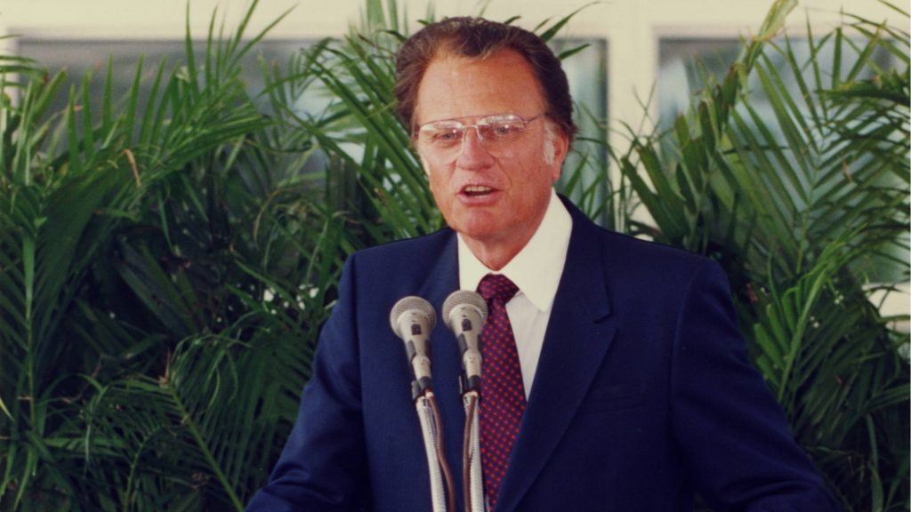 Billy Graham speaking in front of a podium with microphones