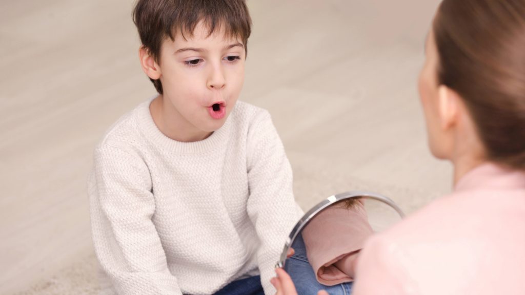 Un niño recibe terapia del lenguaje con una terapeuta que usa un espejo