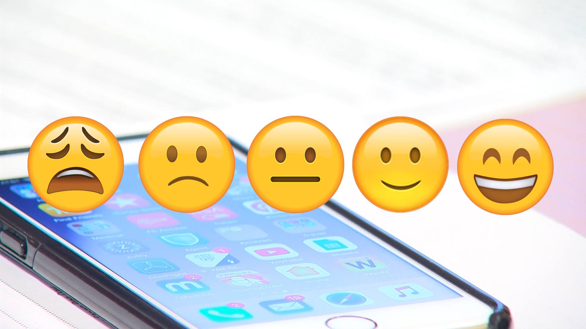 A screen shot of five emojis with a cell phone in the background.