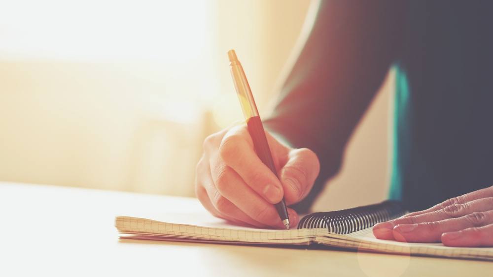 Unas manos femeninas sostiene un bolígrafo para escribir en una libreta 