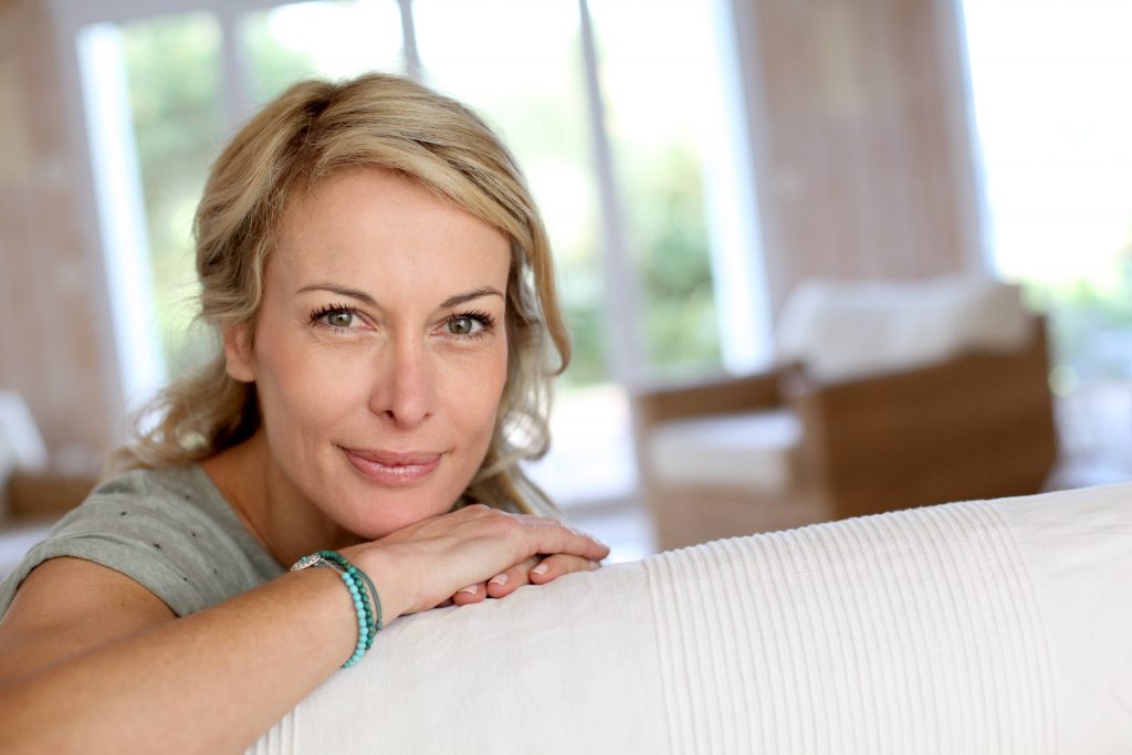 a close-up of a smiling middle-aged woman looking over the back of a couch