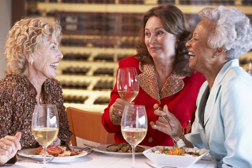 three older women, talking and laughing over dinner and wine