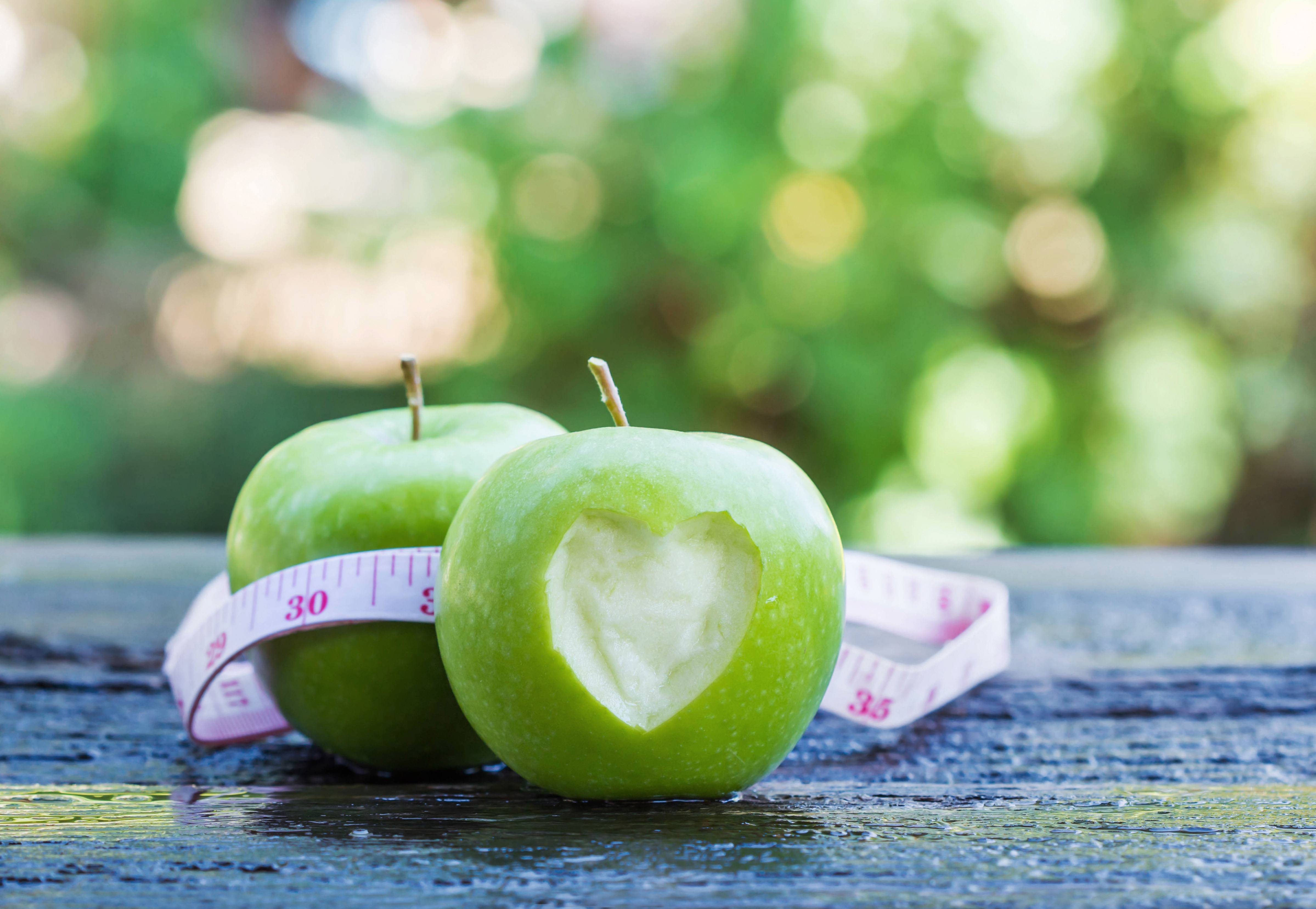 green apples with a heart carved in the skin and a tape measure around the apple representing weightloss and healthy eating