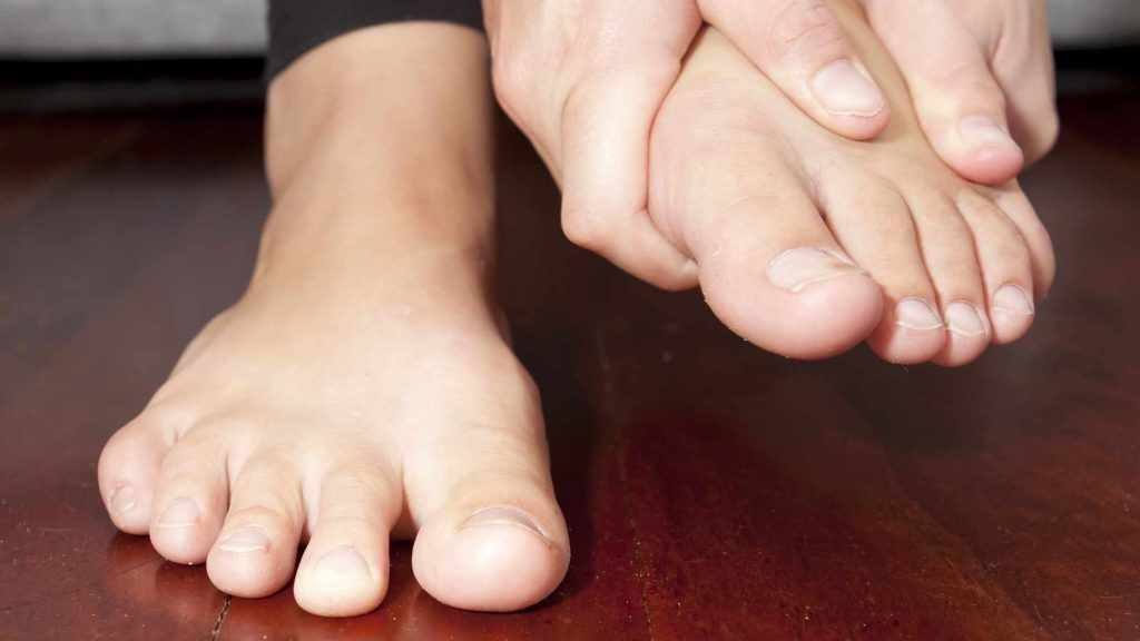 a closeup of person barefoot showing toes and two feet, one on the floor and the other held in the person's hands