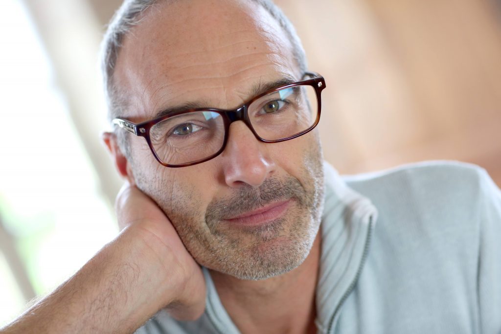 a close-up of a smiling middle-aged man, wearing glasses, resting his cheek on his hand
