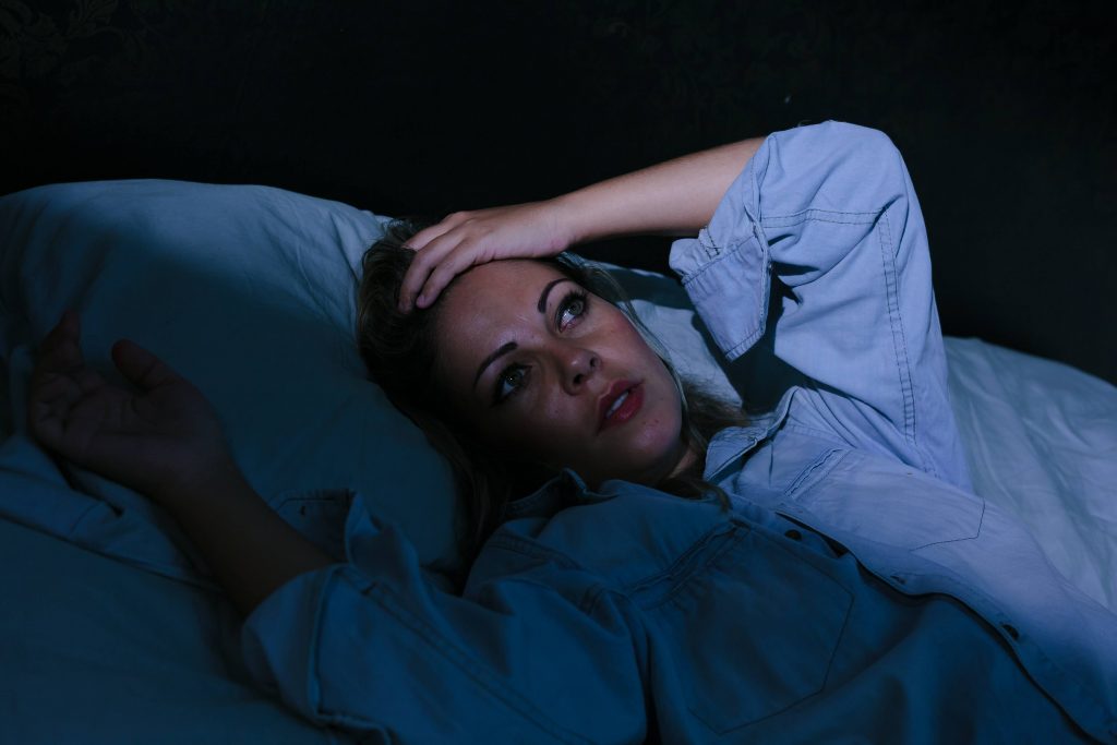 a young woman in a dark bedroom, lying in bed with her eyes open and her hand to her forehead, suffering from insomnia or stress