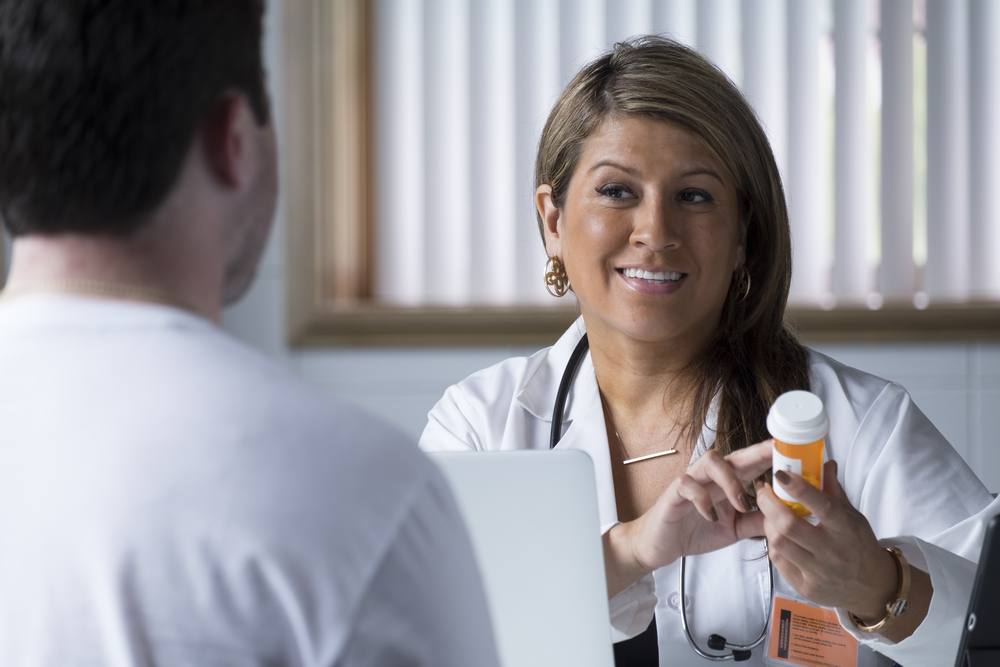 Hispanic woman doctor talking to male patient with prescription bottle