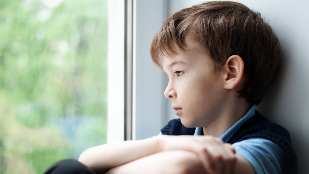 a sad, depressed, upset, unhappy little boy sitting near a window and looking out