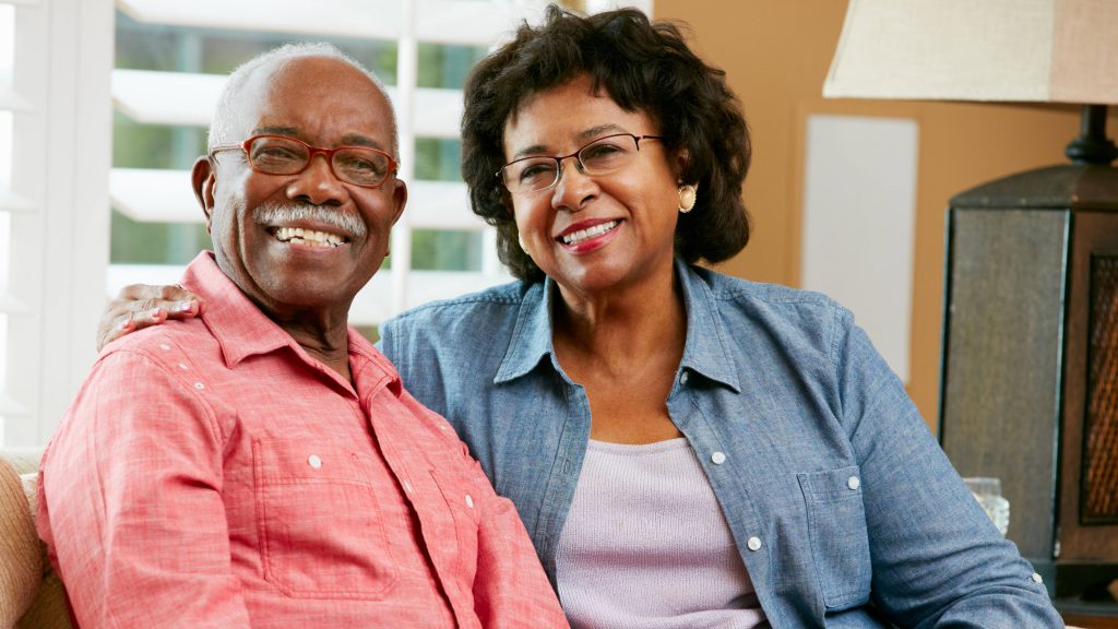 a smiling older couple at home, sitting together on a couch, aging is a risk for heart disease and stroke
