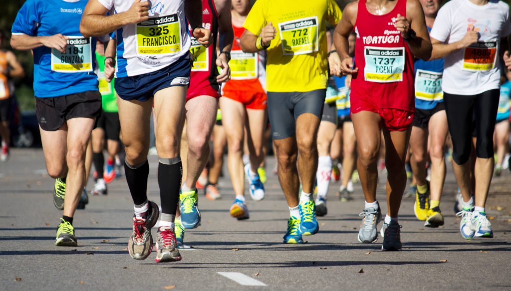 legs and feet of a large group of runners in a marathon race on pavement or a road