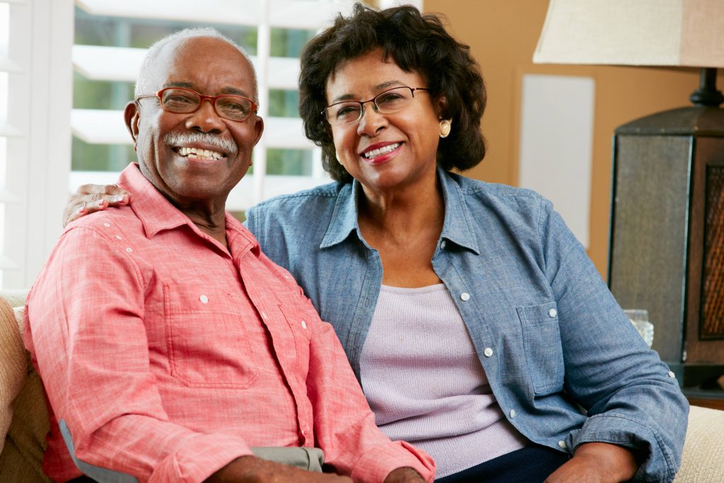 a smiling older couple at home, sitting together on a couch
