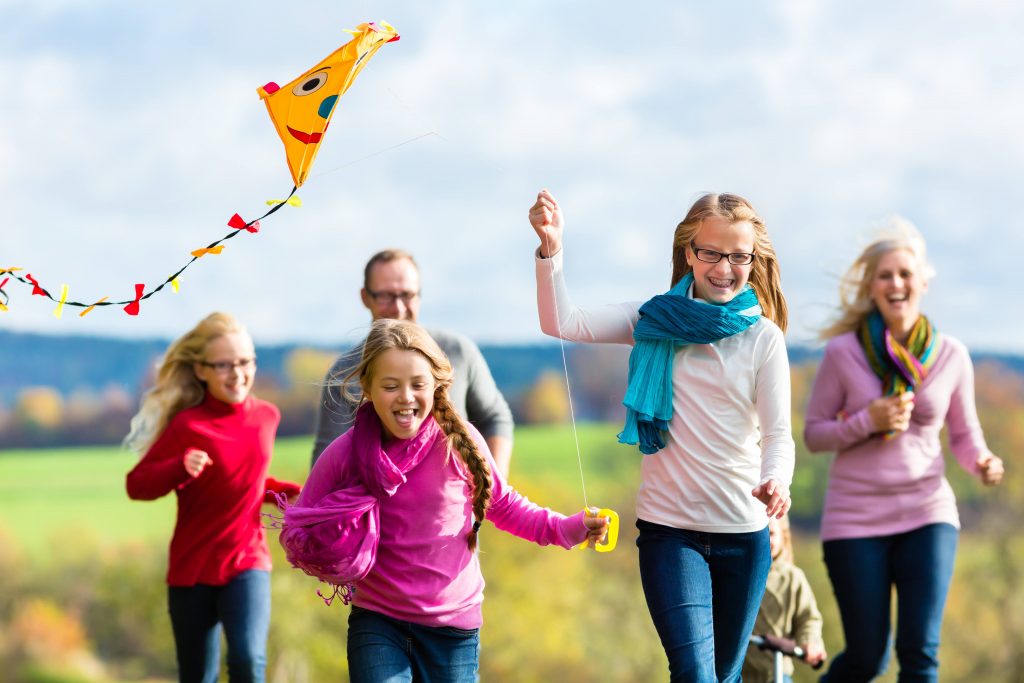 a family - parents and young children - running outside, flying a kite, laughing