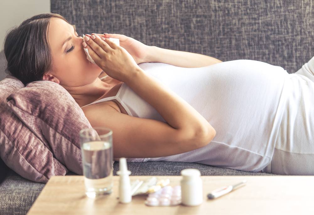 a young pregnant woman on a couch, with medicine and coughing, sneezing looking like she's sick or ill with a cold, flu, or allergies