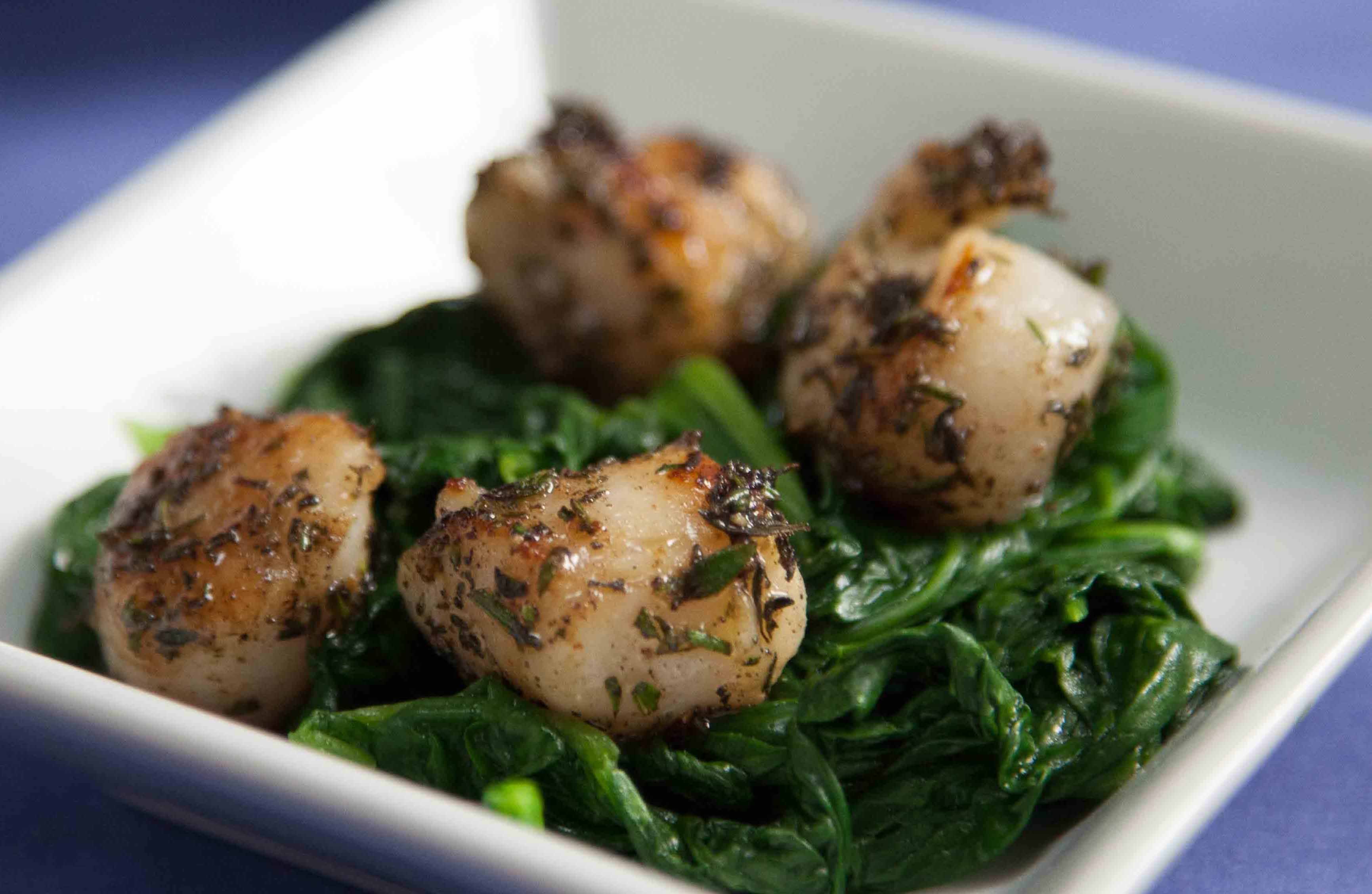 a white bowl with seared scallops and green vegetables