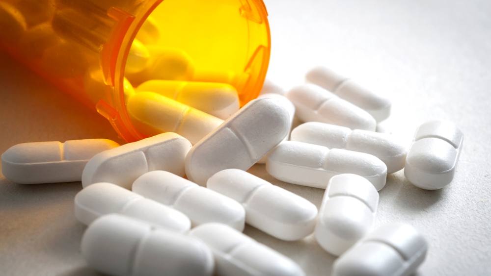Imagen de un frasco de medicamentos recetados del cual salen unas pastillas de hidrocodona.