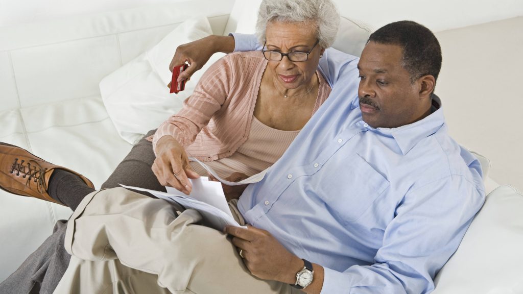 a middle-aged African-American couple sitting on a couch looking at papers, perhaps medical bills