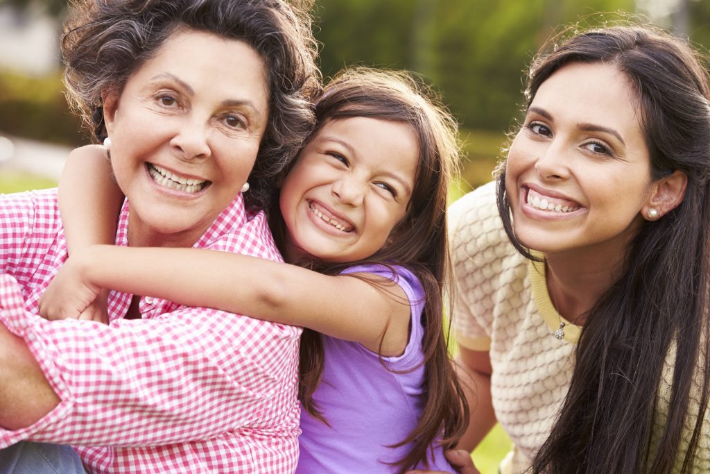 a close-up of three generations - grandmother, daughter and granddaughter - outdoors, smiling, hugging