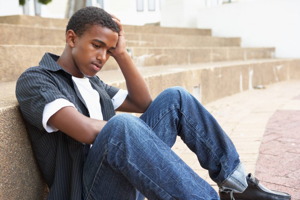 a teenage boy sitting on some steps with this head resting on his hand, looking sad or depressed