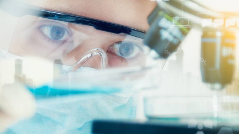 closeup of a researcher wearing protective glasses while looking into a microscope in a lab