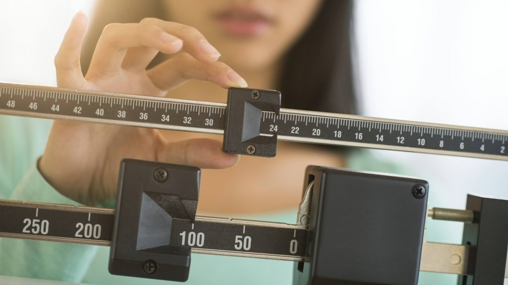a young woman weighing herself and adjust the scale