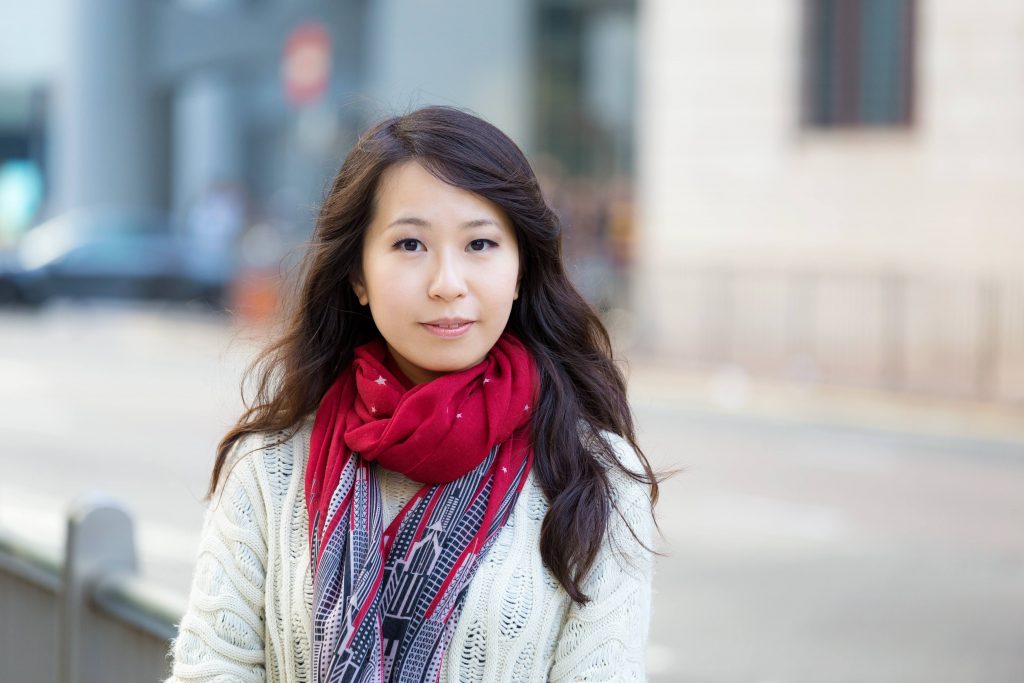 a portrait of a serious-looking young Asian woman wearing brightly-colored scarves around her neck