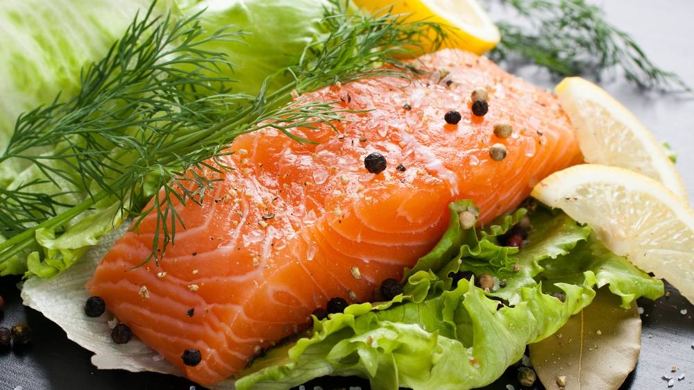 a salmon fillet, rich in omega 3 fish oil, aromatic spices and lemon on fresh lettuce leaves on black wooden background