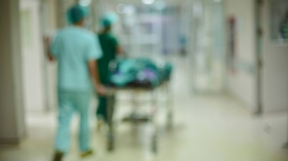 out of focus image of a hospital hallway with medical staff pushing a patient on a gurney