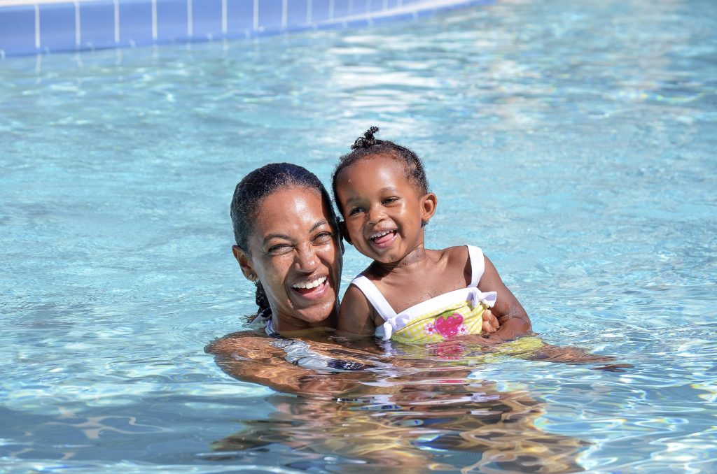 a little girl smiling as a woman, perhaps her mother, holds her in the water of a swimming pool