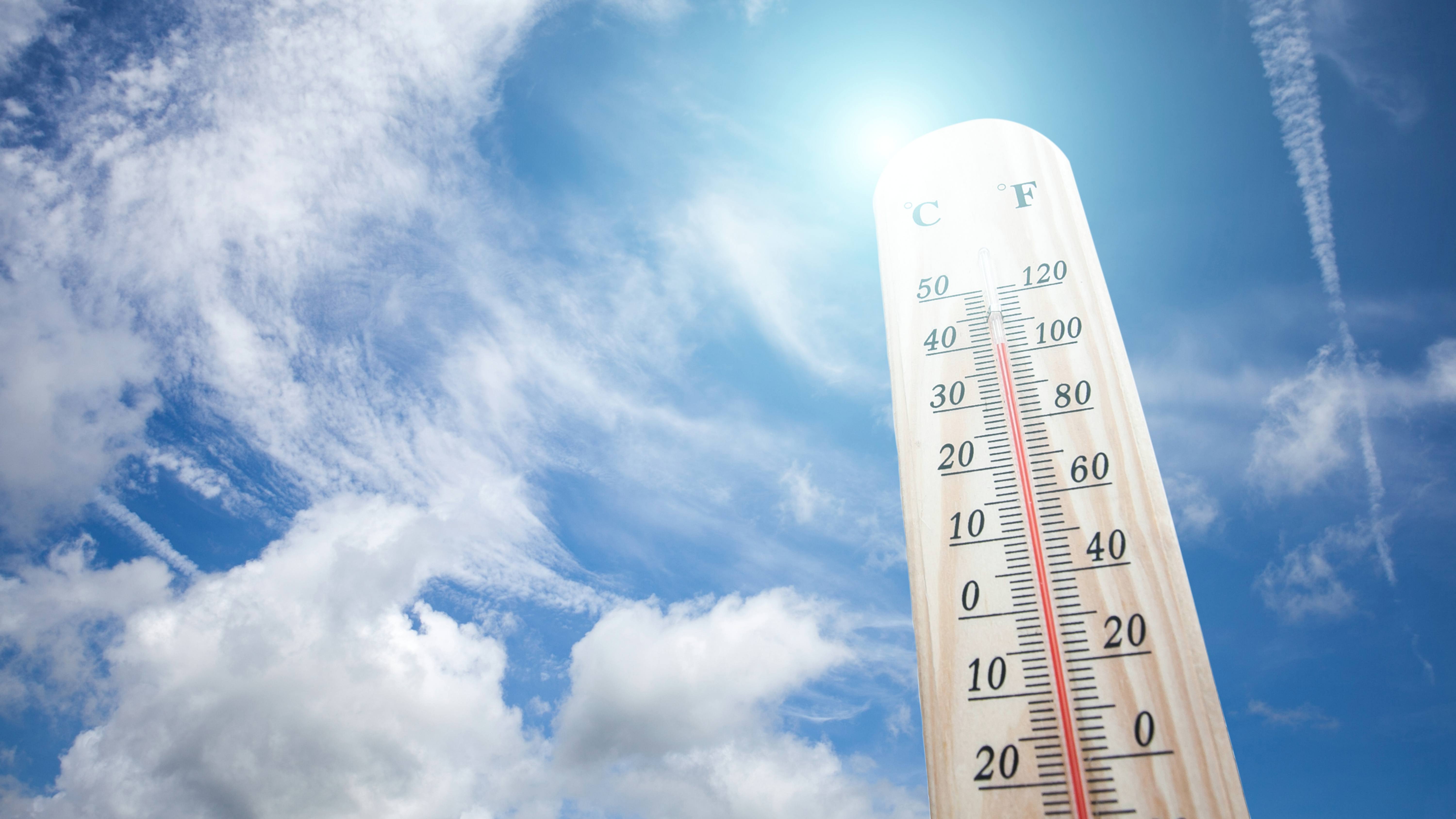 a thermometer on a hot day against a blue sky and sunshine, with high temperature readings, perhaps during a heatwave